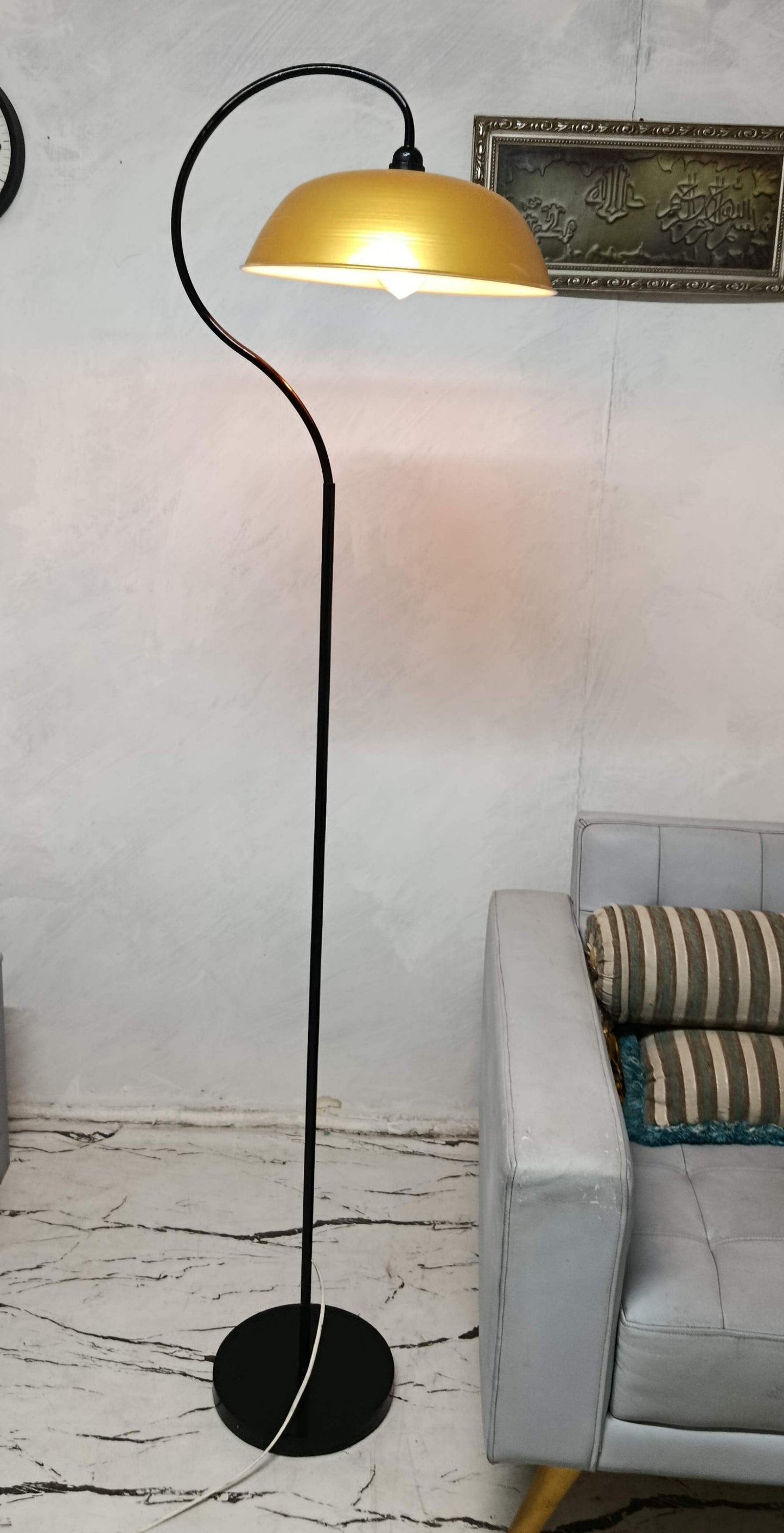 A modern floor lamp with a black metal stand and curved arm, featuring a warm yellow dome shade, shown lit in a living room setting next to a gray sofa.