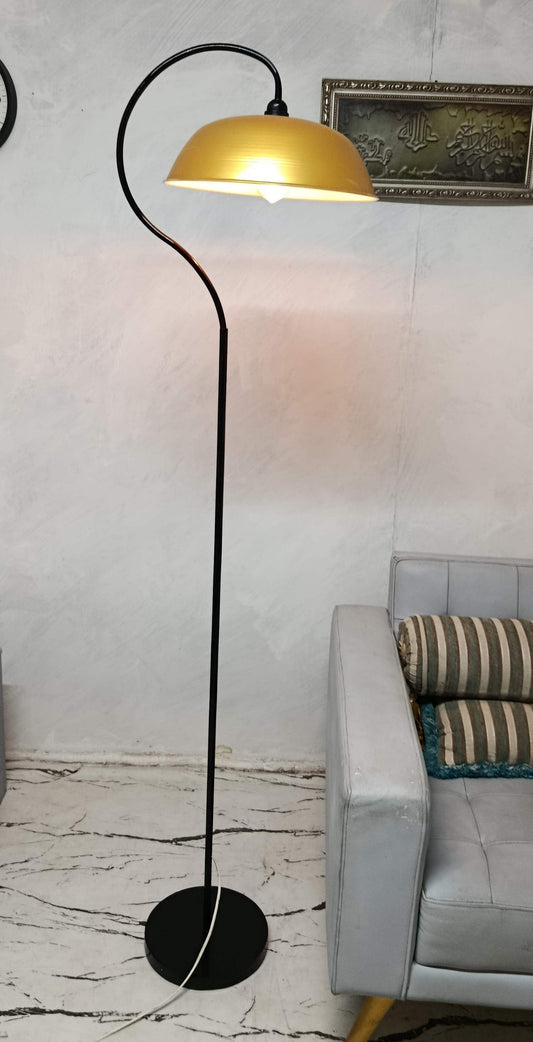A modern floor lamp with a black metal stand and curved arm, featuring a warm yellow dome shade, shown lit in a living room setting next to a gray sofa.
